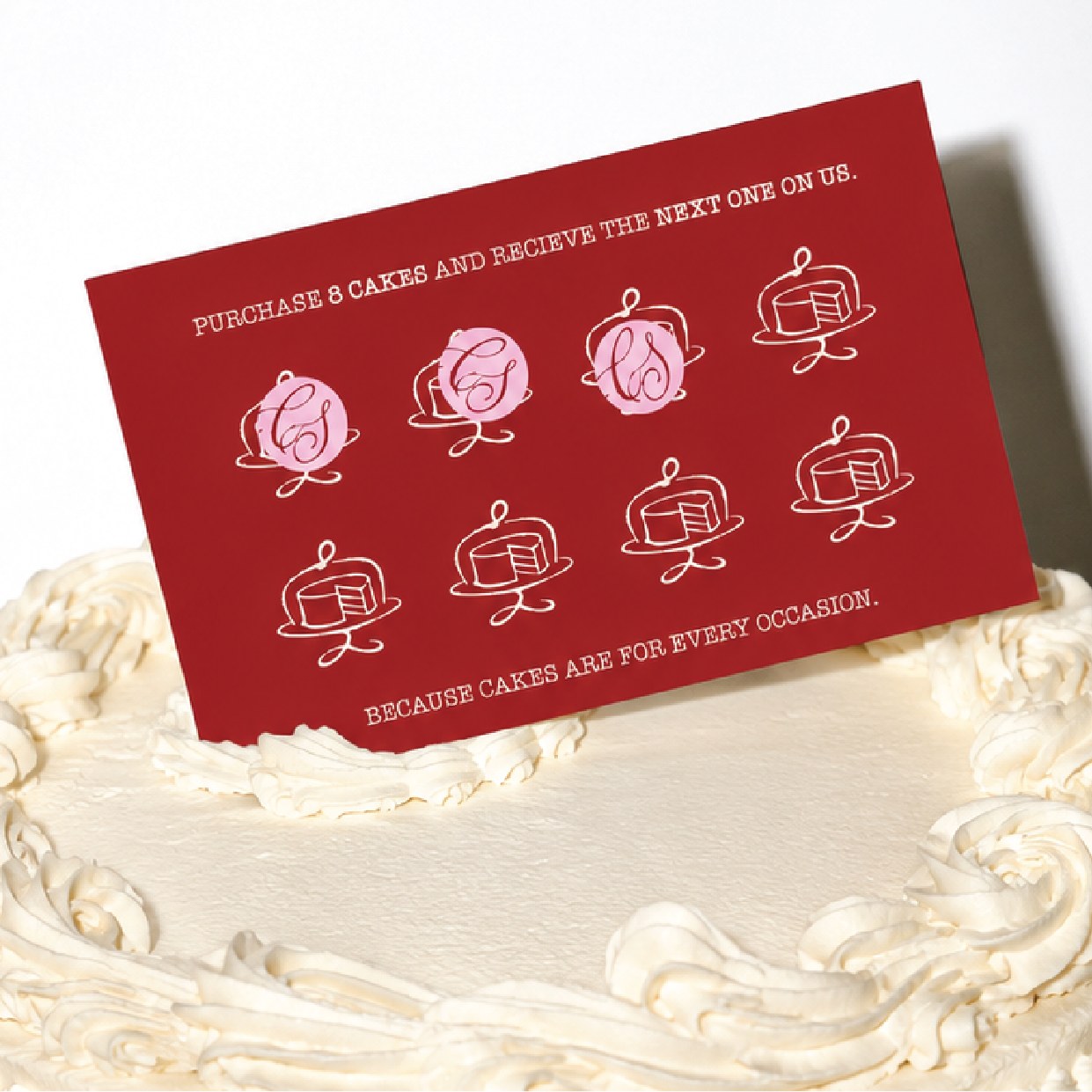 The Cake Social loyalty card propped against a white buttercream cake, three of its eight stands stamped