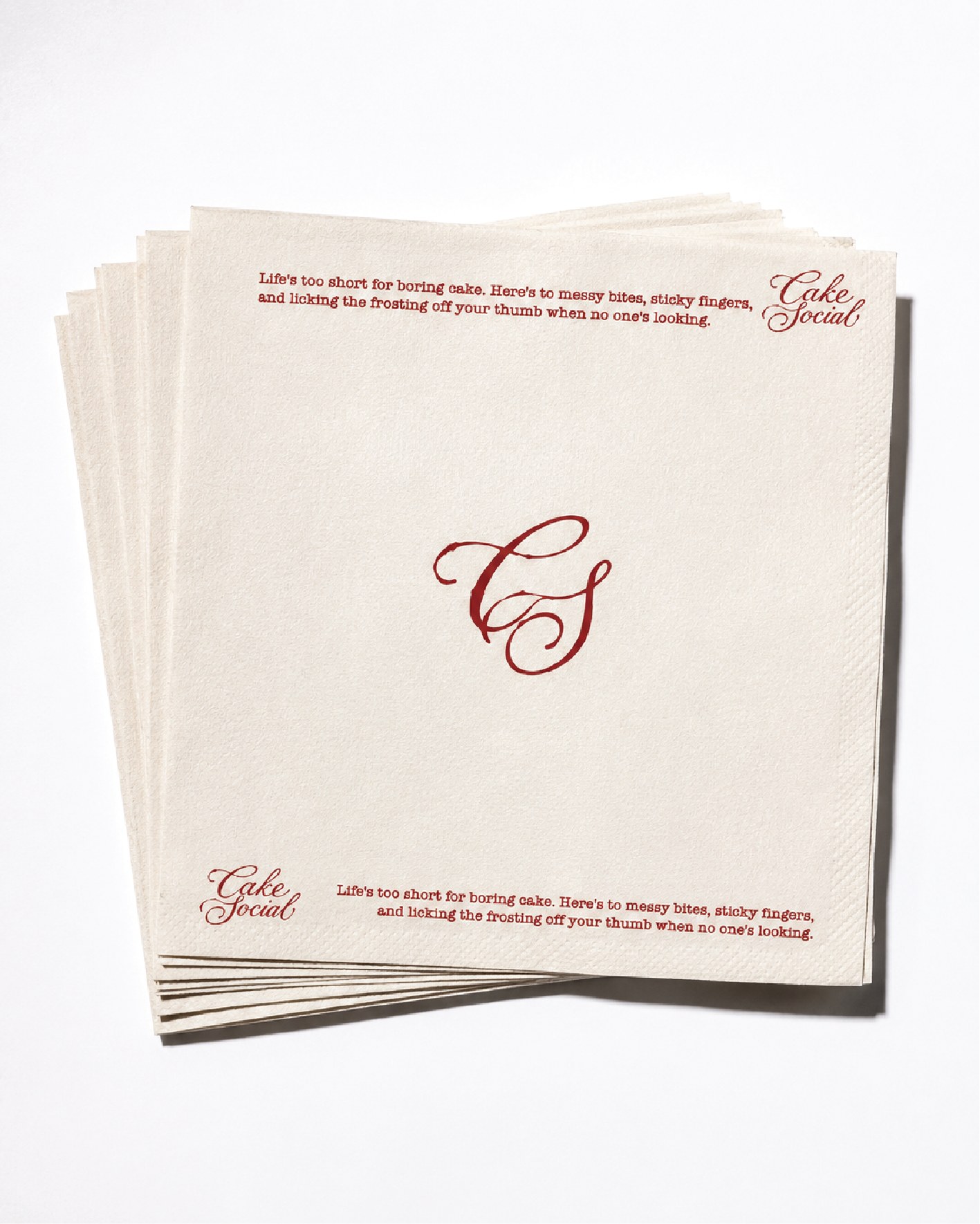 A stack of cream Cake Social napkins with a red CS monogram at centre and copy along the edges