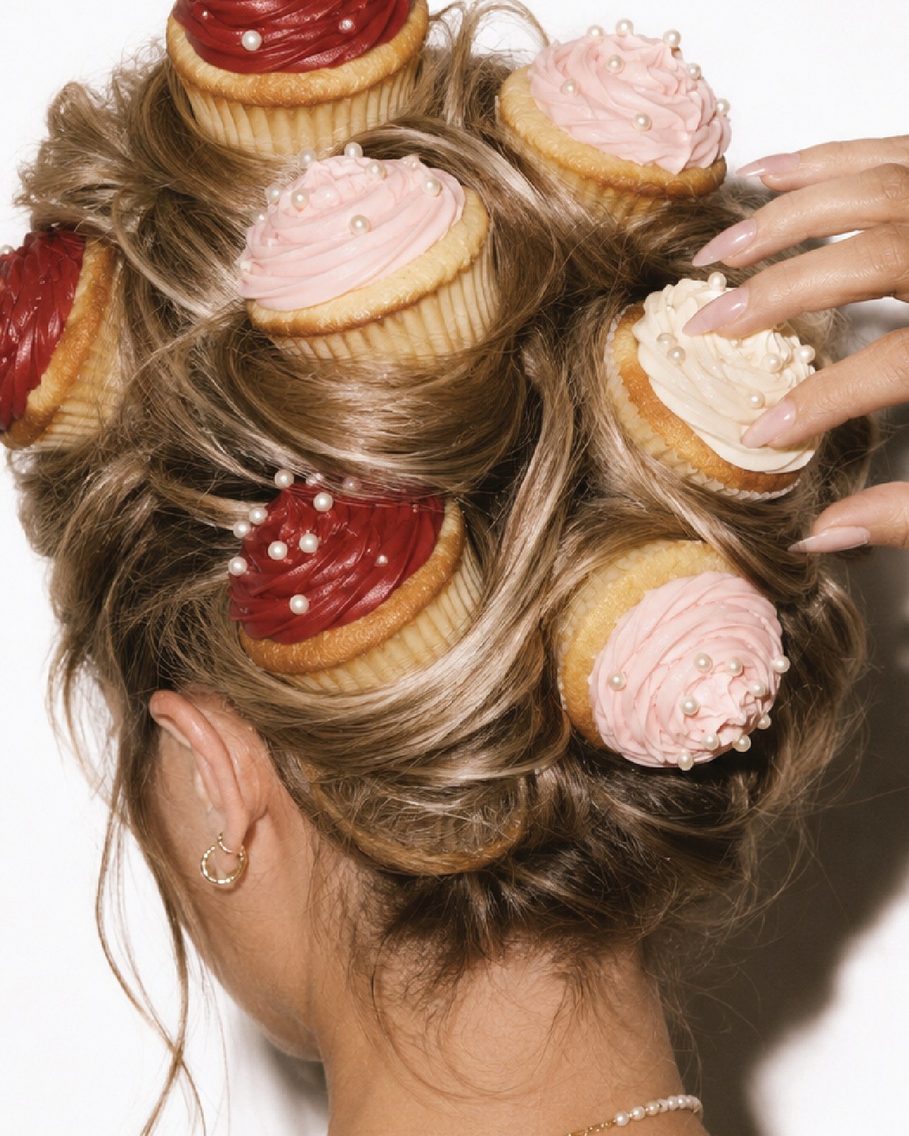 Overhead crop of cupcakes in red, pink and cream pinned into a woman's updo like hair rollers