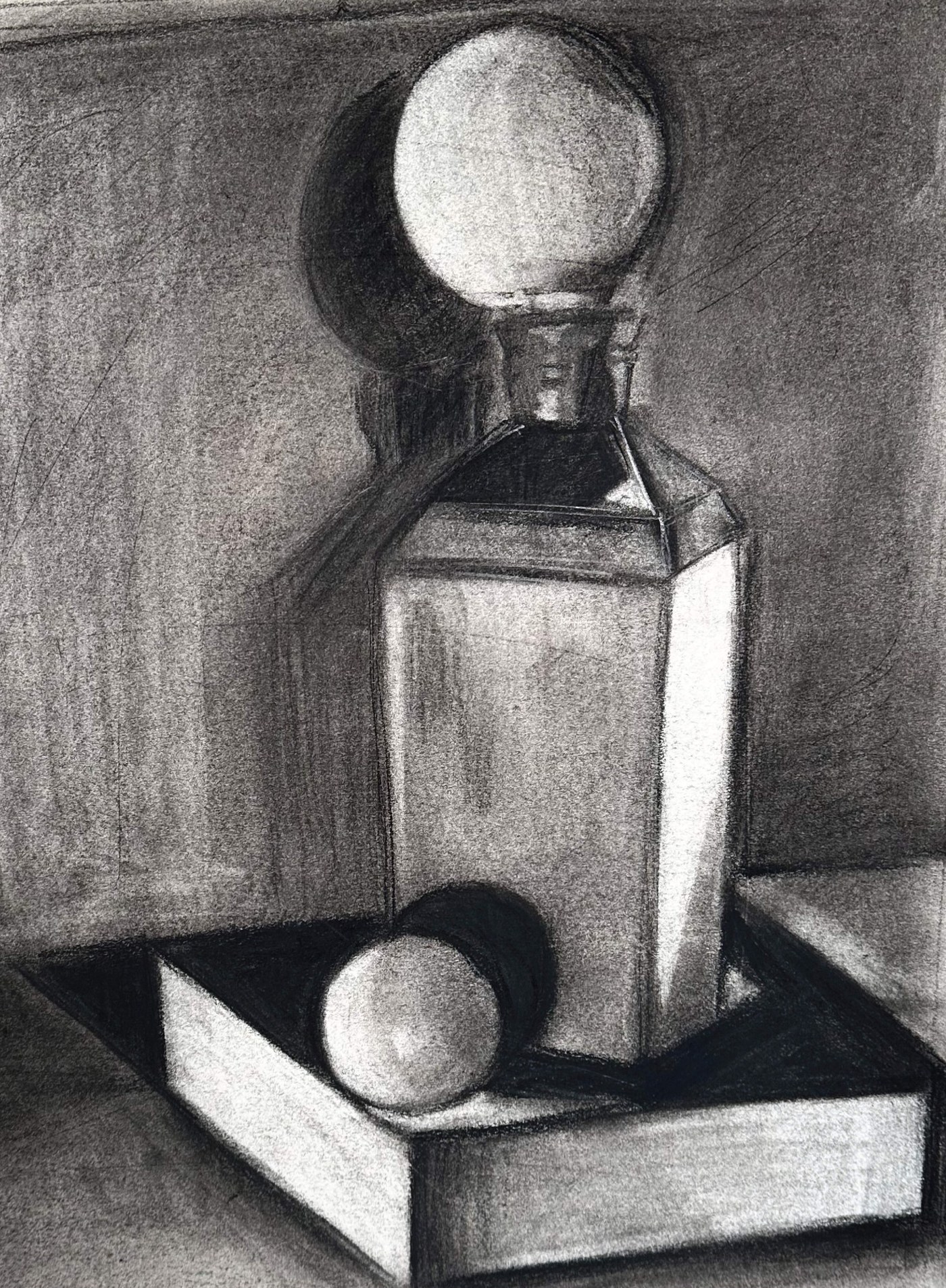 Charcoal still life: a faceted decanter with a round ball stopper standing on a shallow open box, a sphere resting in the box beside it, the stopper throwing a soft round shadow on the wall behind