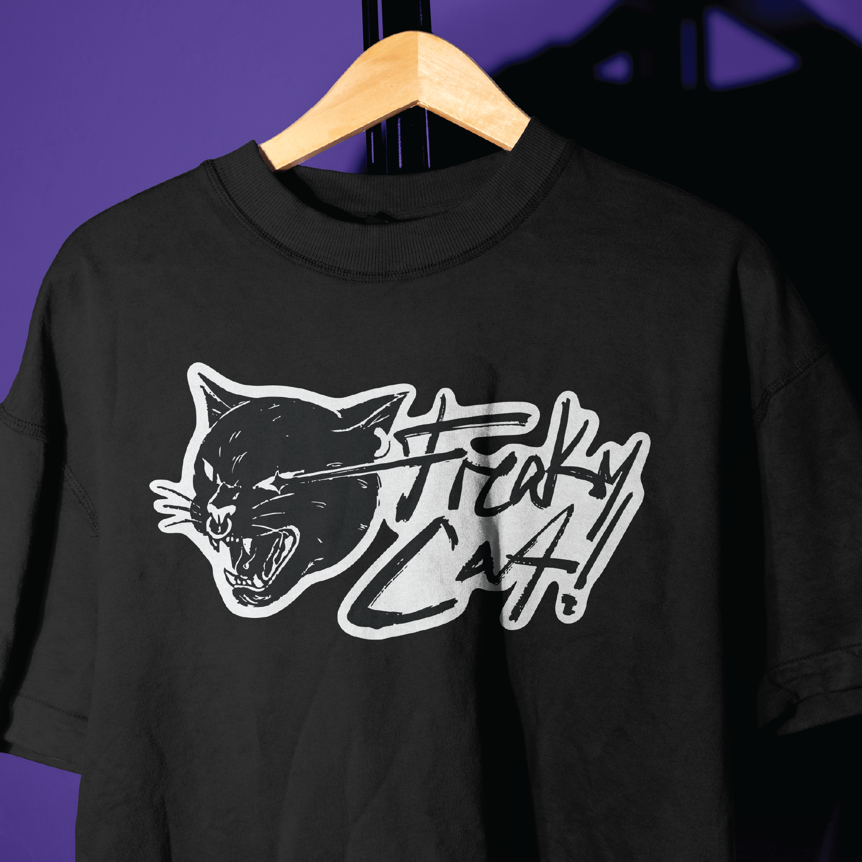 Freaky Cat! black t-shirt on a hanger against a violet wall