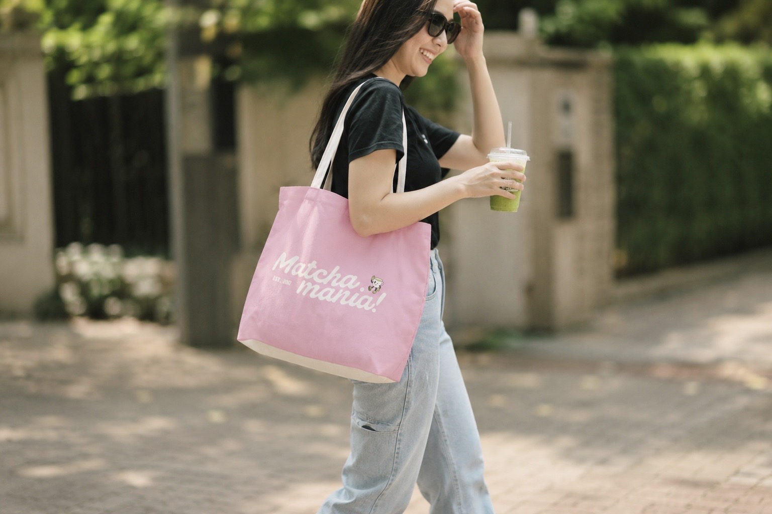 Matcha Mania tote bag carried on the street, with an iced matcha in hand
