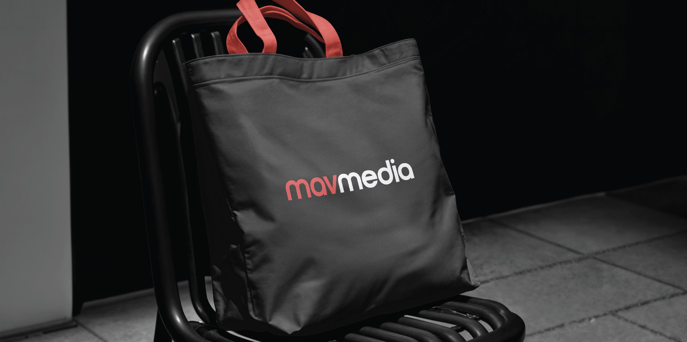 A black Mavmedia tote with red handles resting on a black chair